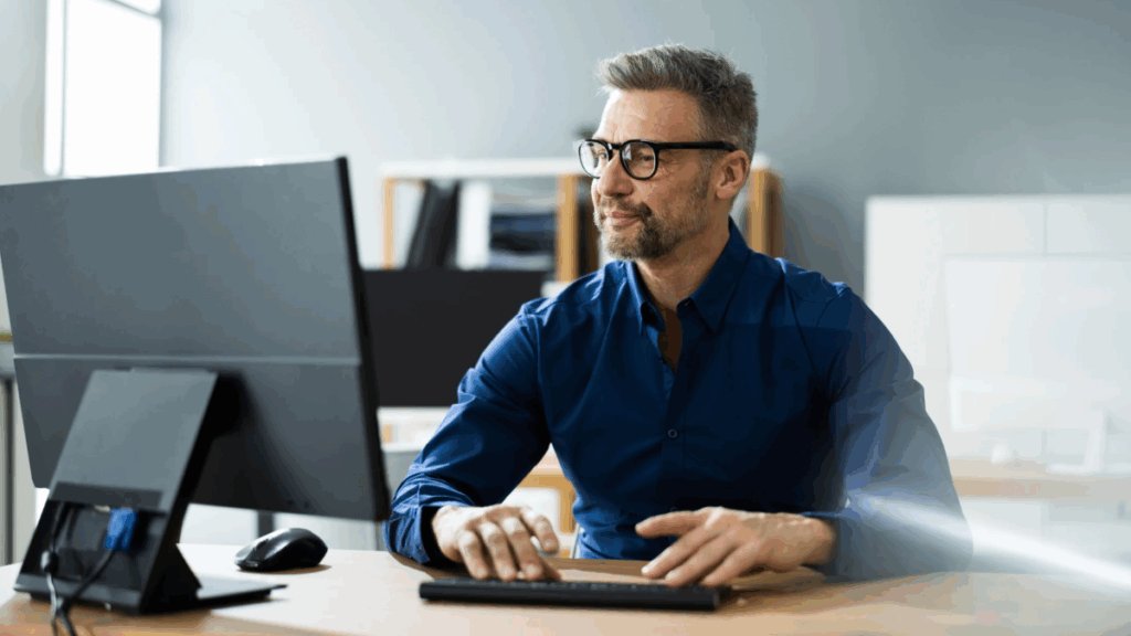 Business professional working at a computer in an office, appearing thoughtful and focused, symbolizing the challenges of managing MCA debt.